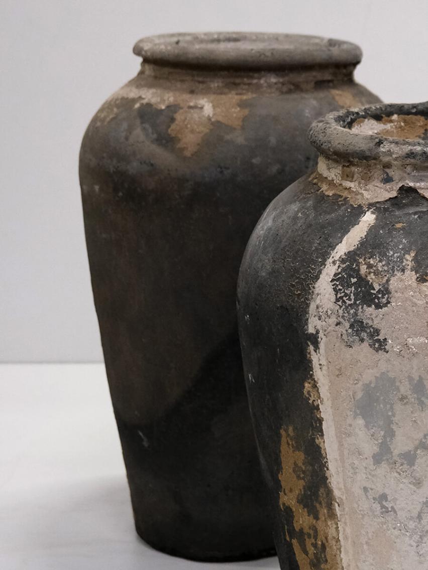 To gamle lerkrukker med rå og patineret overflade, der viser tydelige tegn på slid og autentisk vintage charme, placeret på en neutral baggrund.