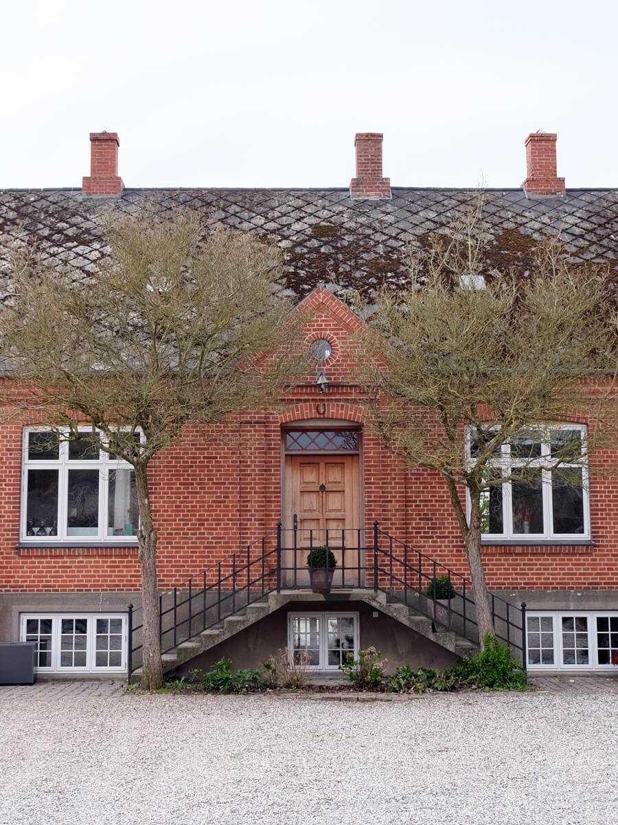 Volleshave Airbnb murstenshus med gråbrunt tag, trædør og trappe op til indgangen.
